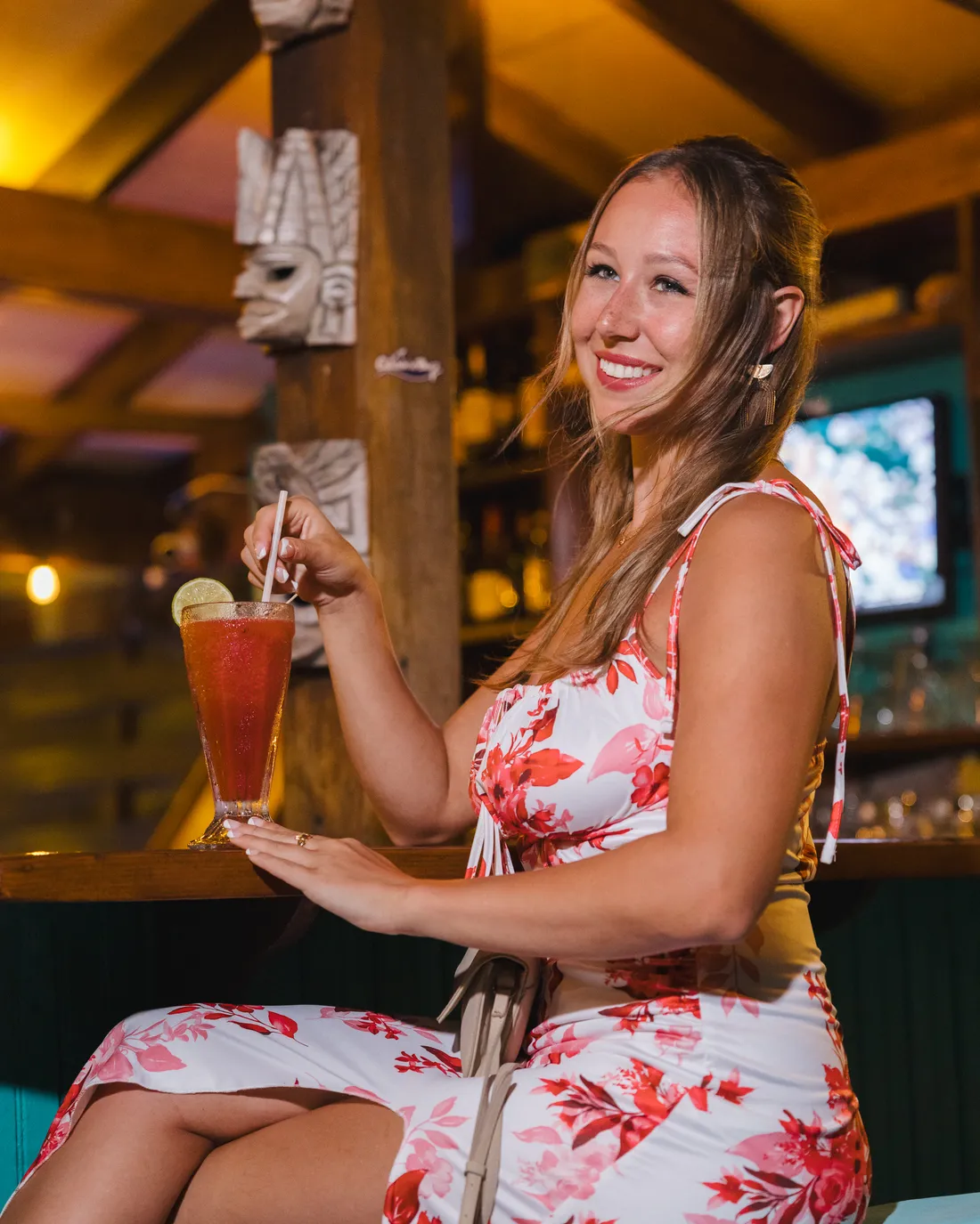 Guest with a cocktail under the tiki masks at the Lazy Pelican at night