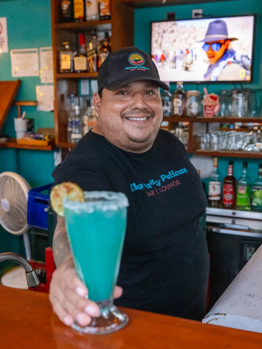 Raymond, bartender at the Lazy Pelican, setting a bright blue cocktail on the bar top