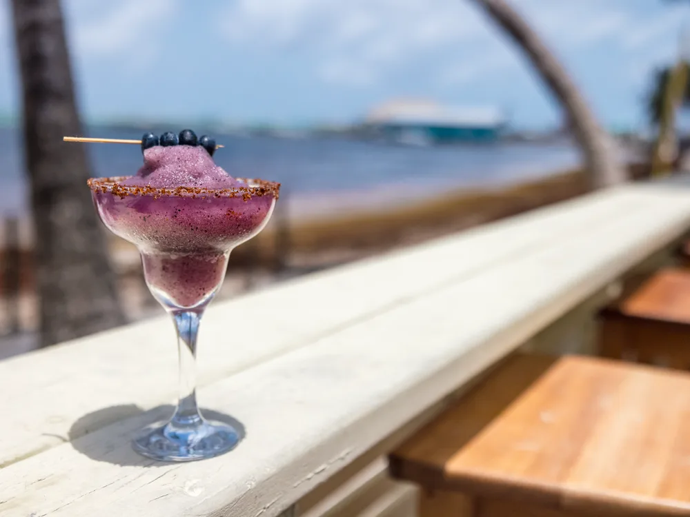 A frozen cocktail resting on the bar rail with the sea behind it