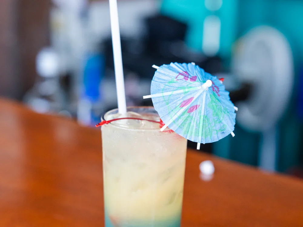 A tall layered cocktail with a paper umbrella on the bar top