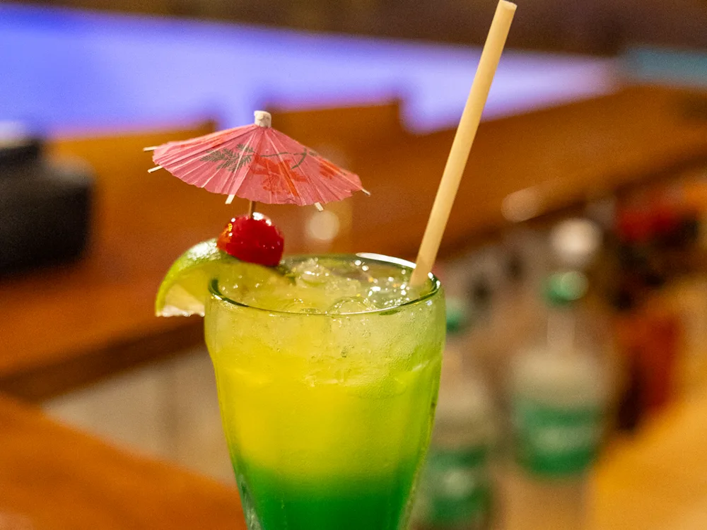 A bright layered cocktail on the bar under the evening lights